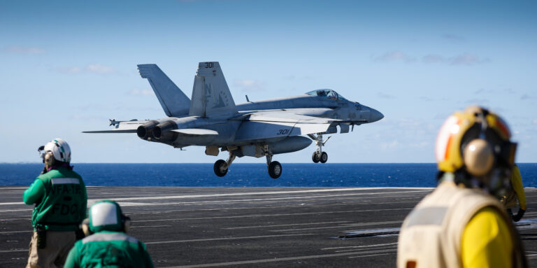 Jet launches from aircraft carrier with crew watching